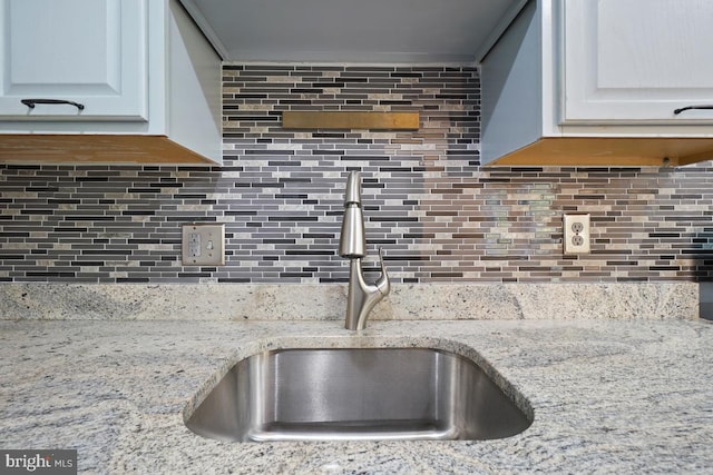 kitchen featuring light stone countertops, white cabinetry, backsplash, and sink