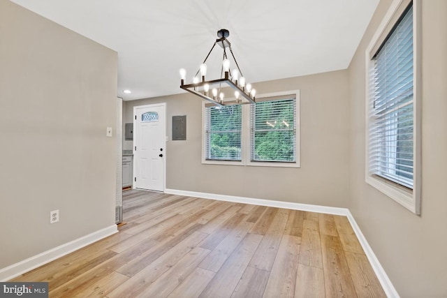 unfurnished dining area featuring light hardwood / wood-style floors, plenty of natural light, electric panel, and an inviting chandelier