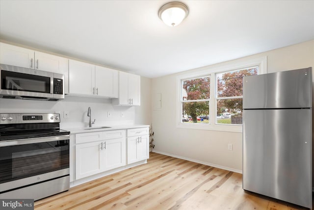 kitchen with white cabinets, stainless steel appliances, light hardwood / wood-style floors, and sink