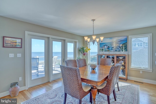 dining space with a water view, an inviting chandelier, and light hardwood / wood-style floors