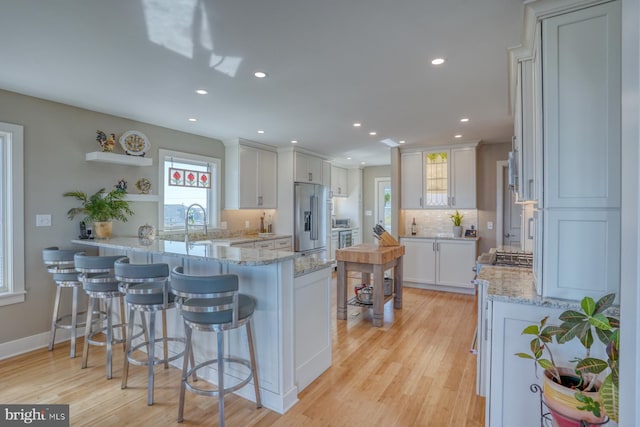 kitchen featuring light wood-type flooring, white cabinetry, kitchen peninsula, and high quality fridge