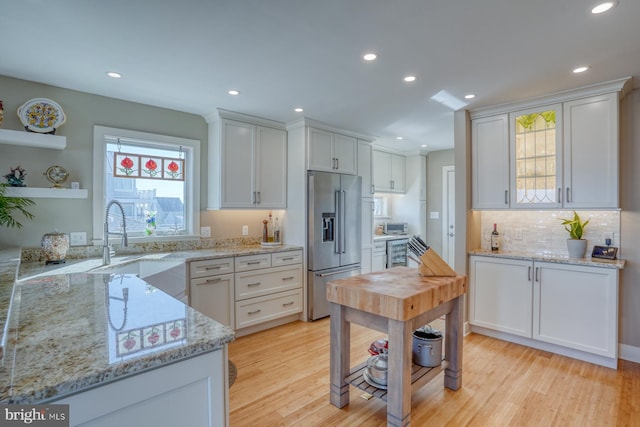 kitchen with white cabinetry, high end refrigerator, light stone counters, backsplash, and light hardwood / wood-style floors