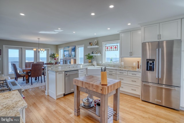 kitchen featuring white cabinetry, an inviting chandelier, decorative light fixtures, appliances with stainless steel finishes, and light wood-type flooring