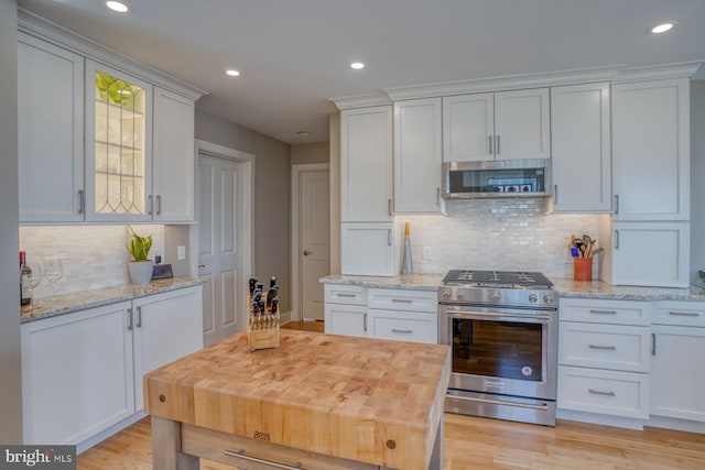 kitchen with white cabinets, light stone counters, stainless steel appliances, and light hardwood / wood-style flooring