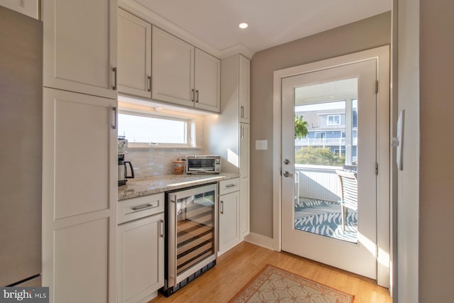 kitchen featuring white cabinets, wine cooler, light stone countertops, tasteful backsplash, and light hardwood / wood-style floors