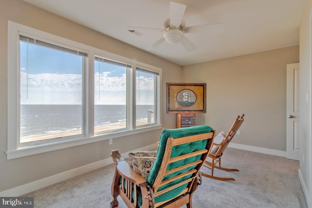 sitting room with ceiling fan, a water view, and light carpet