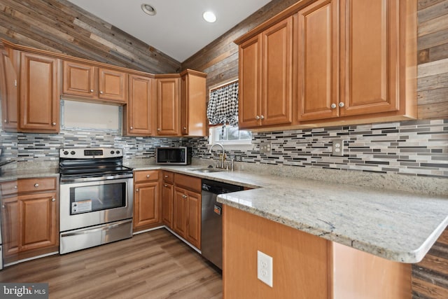 kitchen featuring sink, hardwood / wood-style flooring, light stone countertops, appliances with stainless steel finishes, and kitchen peninsula