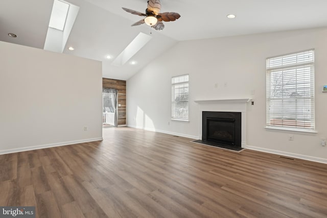 unfurnished living room with wood walls, ceiling fan, dark wood-type flooring, and vaulted ceiling with skylight