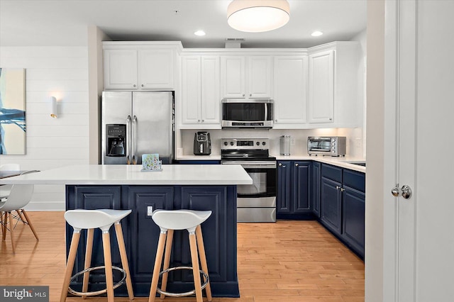 kitchen with white cabinets, blue cabinets, light hardwood / wood-style floors, and appliances with stainless steel finishes