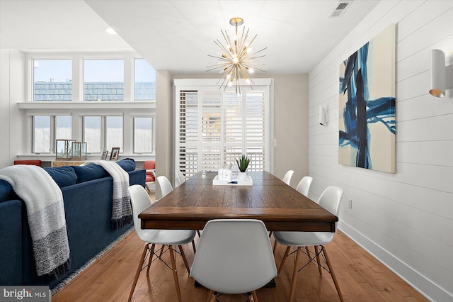 dining room featuring a chandelier, light hardwood / wood-style flooring, and wooden walls