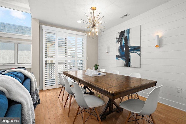 dining space featuring wooden walls, light hardwood / wood-style flooring, and a notable chandelier