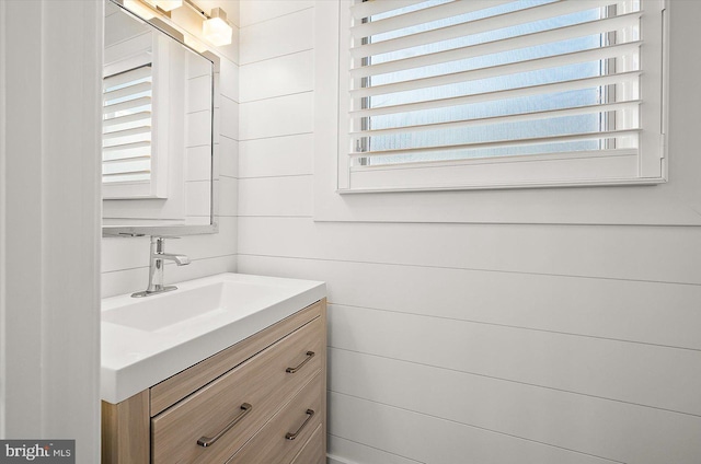 bathroom with a wealth of natural light, vanity, and wood walls