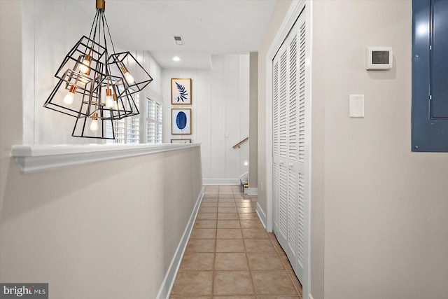 corridor featuring a notable chandelier, light tile patterned floors, and electric panel