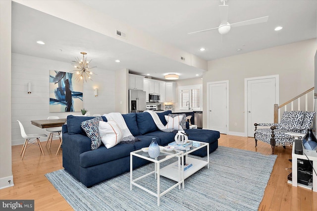 living room featuring wood walls, light hardwood / wood-style flooring, and ceiling fan with notable chandelier