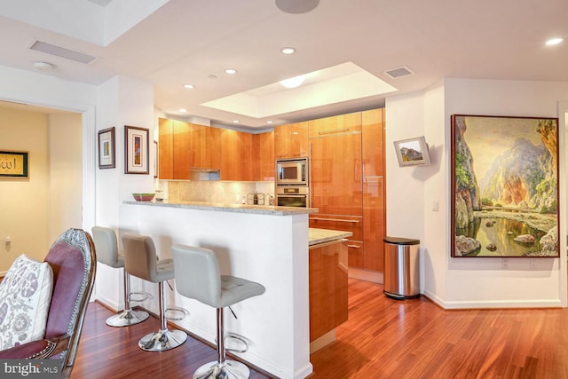 kitchen featuring stainless steel appliances, kitchen peninsula, decorative backsplash, and light wood-type flooring