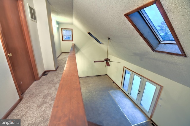 bonus room featuring ceiling fan, vaulted ceiling with skylight, light colored carpet, and a textured ceiling