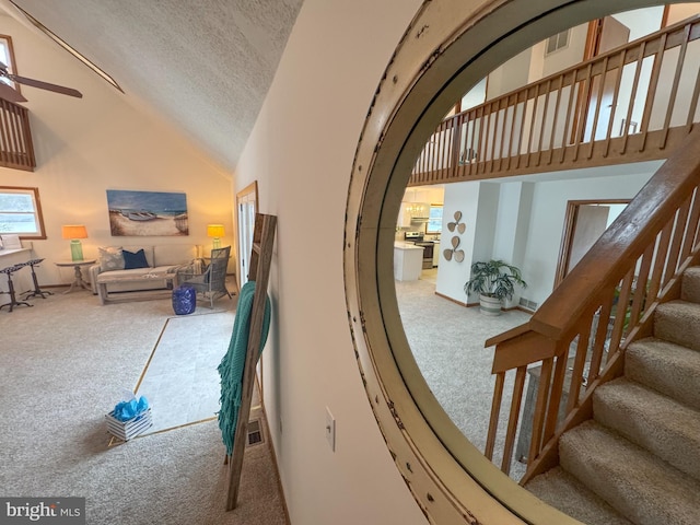 stairway with ceiling fan, carpet floors, a textured ceiling, and high vaulted ceiling