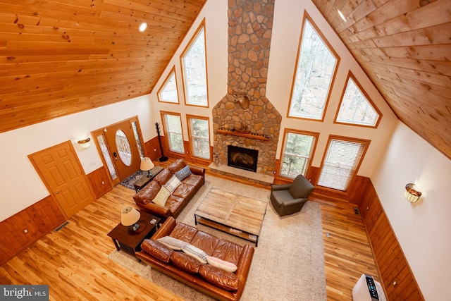 living room featuring wood ceiling, wooden walls, light hardwood / wood-style flooring, high vaulted ceiling, and a stone fireplace