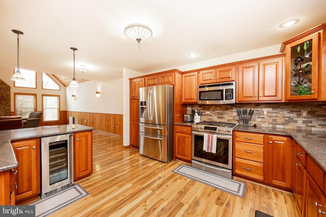 kitchen with beverage cooler, decorative light fixtures, wooden walls, appliances with stainless steel finishes, and light wood-type flooring