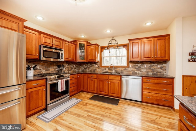 kitchen featuring light hardwood / wood-style floors, sink, stainless steel appliances, and dark stone counters