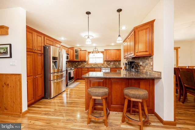 kitchen with sink, stainless steel appliances, light hardwood / wood-style flooring, kitchen peninsula, and a breakfast bar