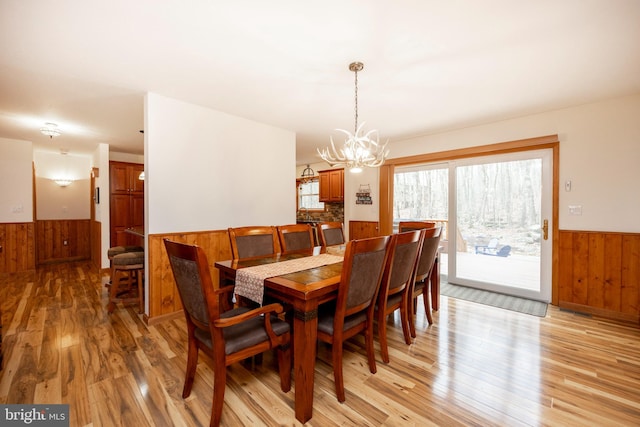 dining space with an inviting chandelier, light hardwood / wood-style flooring, and wooden walls