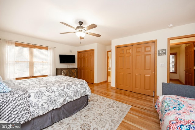 bedroom with ceiling fan, light wood-type flooring, and two closets