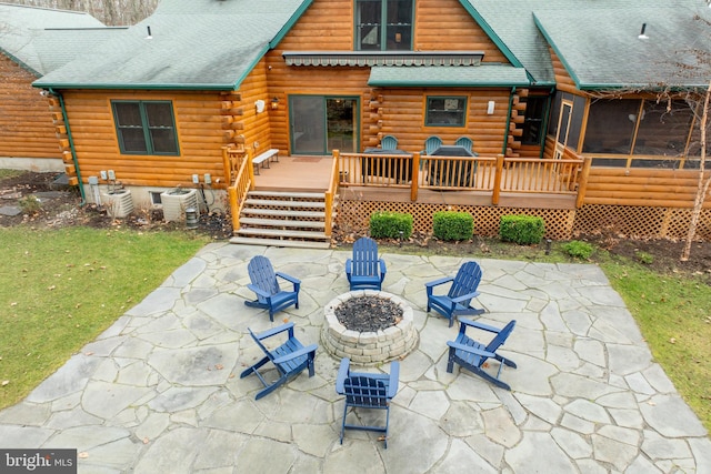 rear view of property featuring a sunroom, a fire pit, central air condition unit, a wooden deck, and a patio area