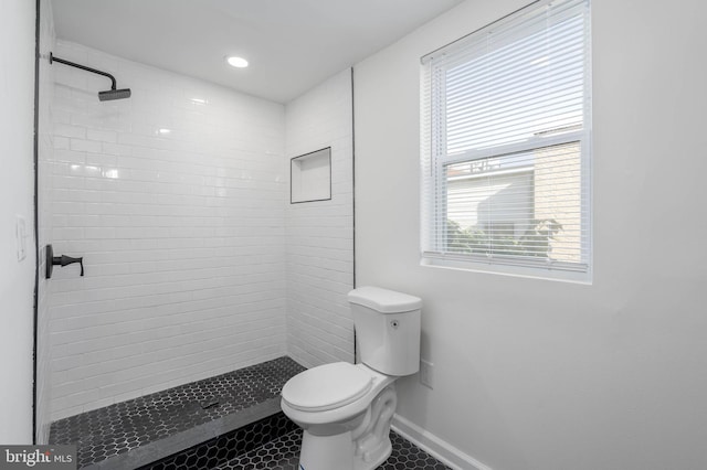 bathroom with a tile shower, tile patterned flooring, a healthy amount of sunlight, and toilet