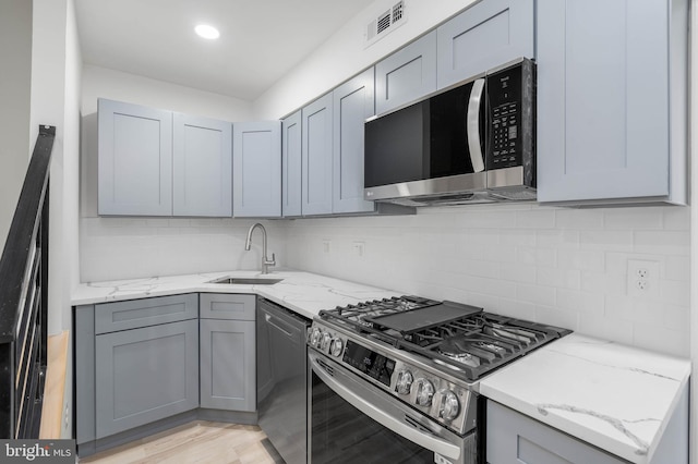 kitchen featuring light stone counters, sink, appliances with stainless steel finishes, and light hardwood / wood-style flooring