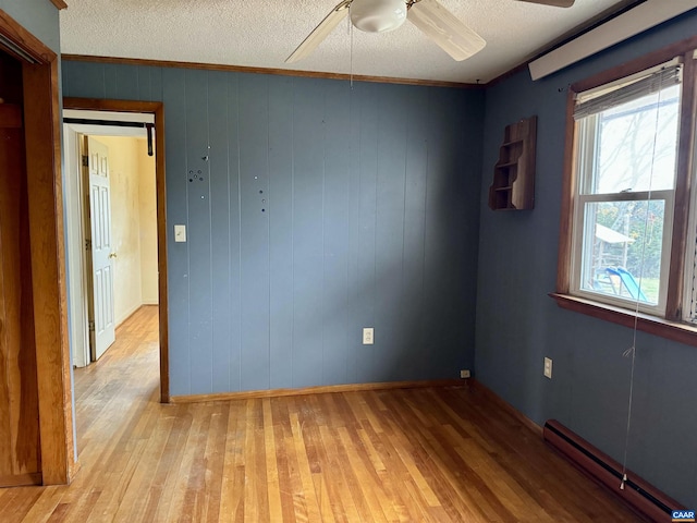 unfurnished room with wooden walls, light hardwood / wood-style floors, crown molding, and a baseboard heating unit