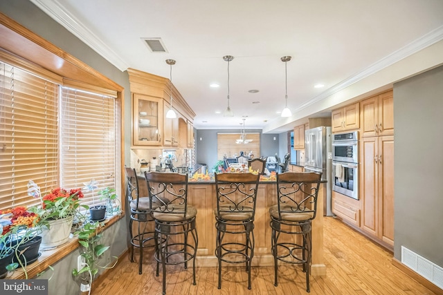 kitchen featuring kitchen peninsula, double oven, crown molding, pendant lighting, and light hardwood / wood-style floors