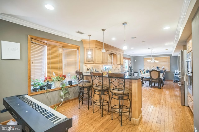 kitchen featuring decorative light fixtures, a kitchen bar, light wood-type flooring, and crown molding