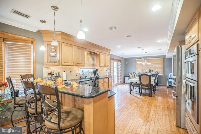 kitchen with kitchen peninsula, a kitchen breakfast bar, crown molding, decorative light fixtures, and light hardwood / wood-style flooring