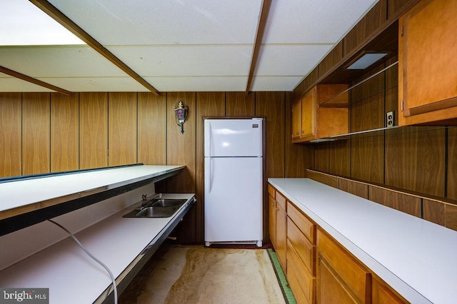 kitchen with sink, white fridge, and wood walls