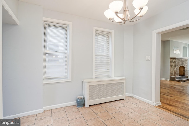 interior space featuring radiator heating unit, light wood-type flooring, a stone fireplace, and a notable chandelier