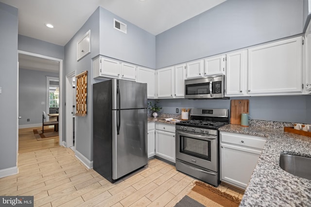 kitchen with white cabinets, stainless steel appliances, light stone counters, and light hardwood / wood-style floors