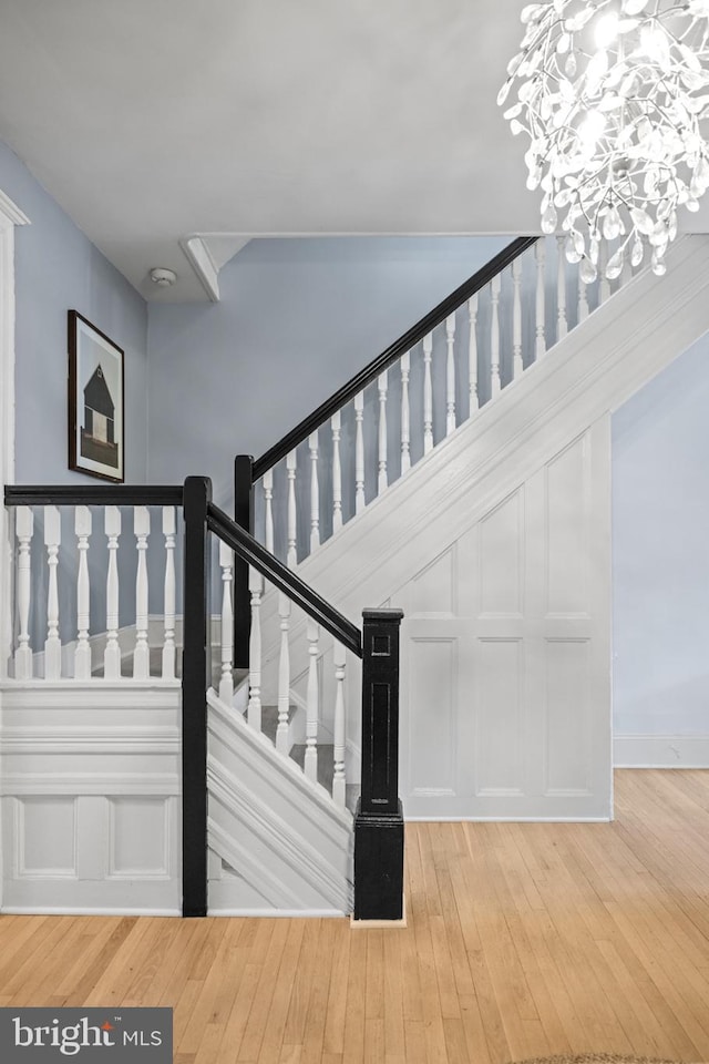 stairway with hardwood / wood-style floors and an inviting chandelier