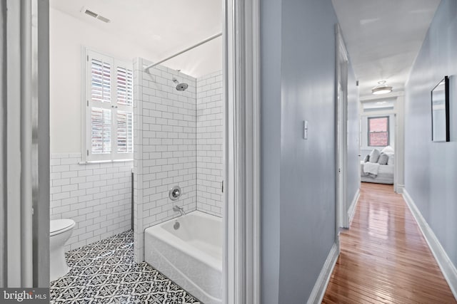 bathroom featuring hardwood / wood-style flooring, tiled shower / bath combo, toilet, and a wealth of natural light