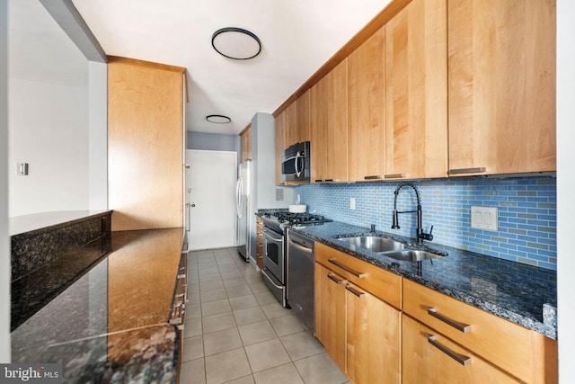 kitchen featuring sink, backsplash, dark stone counters, light tile patterned flooring, and appliances with stainless steel finishes