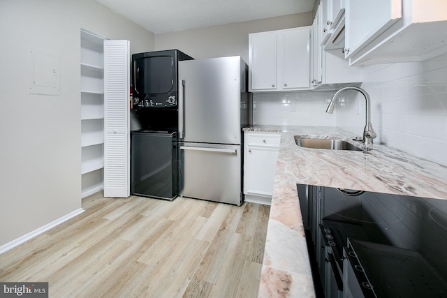 kitchen featuring stainless steel refrigerator, sink, white cabinets, stacked washer and clothes dryer, and light wood-type flooring