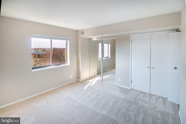 unfurnished bedroom featuring light colored carpet, a textured ceiling, and a closet