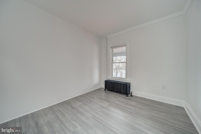 spare room featuring radiator heating unit, ornamental molding, and light wood-type flooring