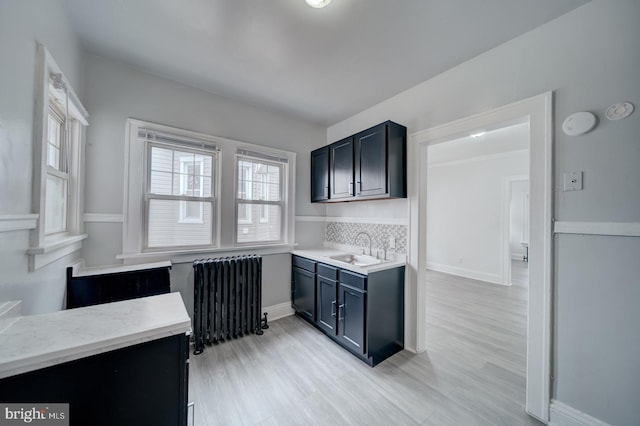 kitchen with radiator, sink, decorative backsplash, and light wood-type flooring