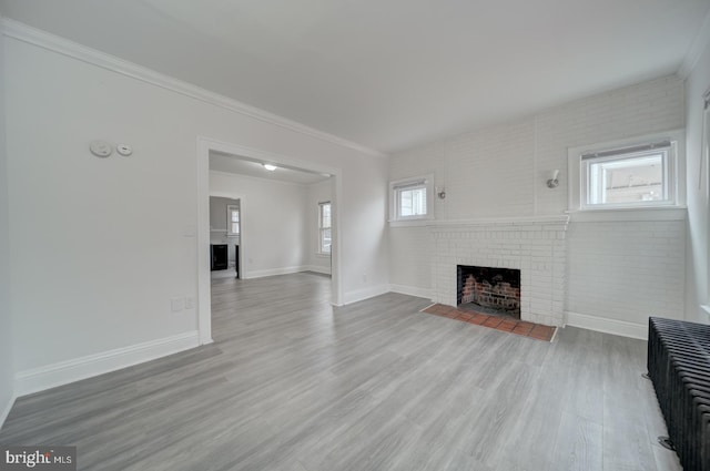 unfurnished living room featuring brick wall, ornamental molding, a brick fireplace, and light hardwood / wood-style floors