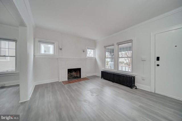 unfurnished living room with radiator, crown molding, a brick fireplace, and light wood-type flooring