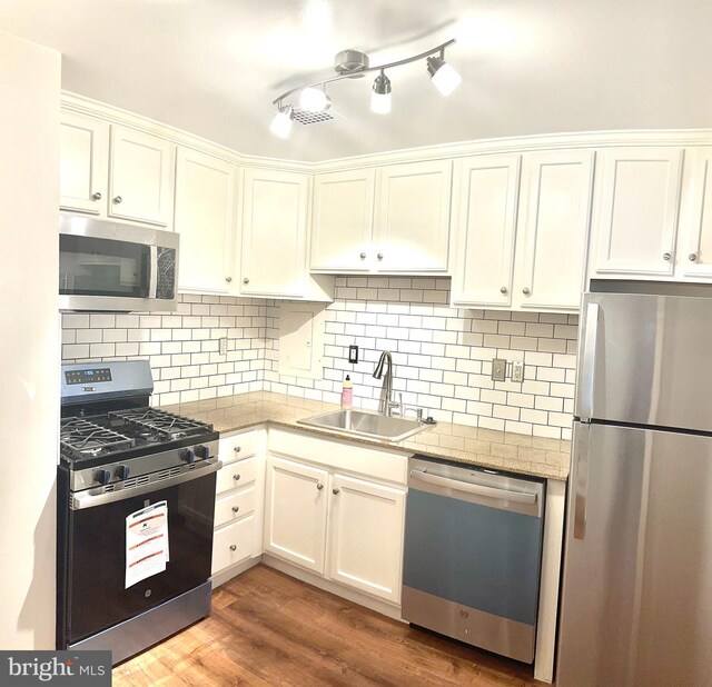 kitchen with tasteful backsplash, stainless steel appliances, sink, hardwood / wood-style floors, and white cabinetry