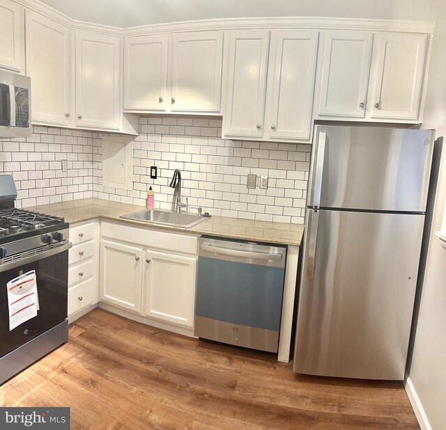 kitchen featuring appliances with stainless steel finishes, light wood-type flooring, backsplash, sink, and white cabinetry