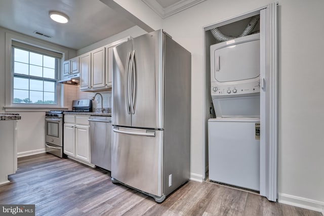 kitchen with tasteful backsplash, stainless steel appliances, wood-type flooring, stacked washer and dryer, and white cabinetry