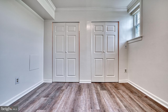 unfurnished bedroom featuring wood-type flooring, crown molding, and multiple closets